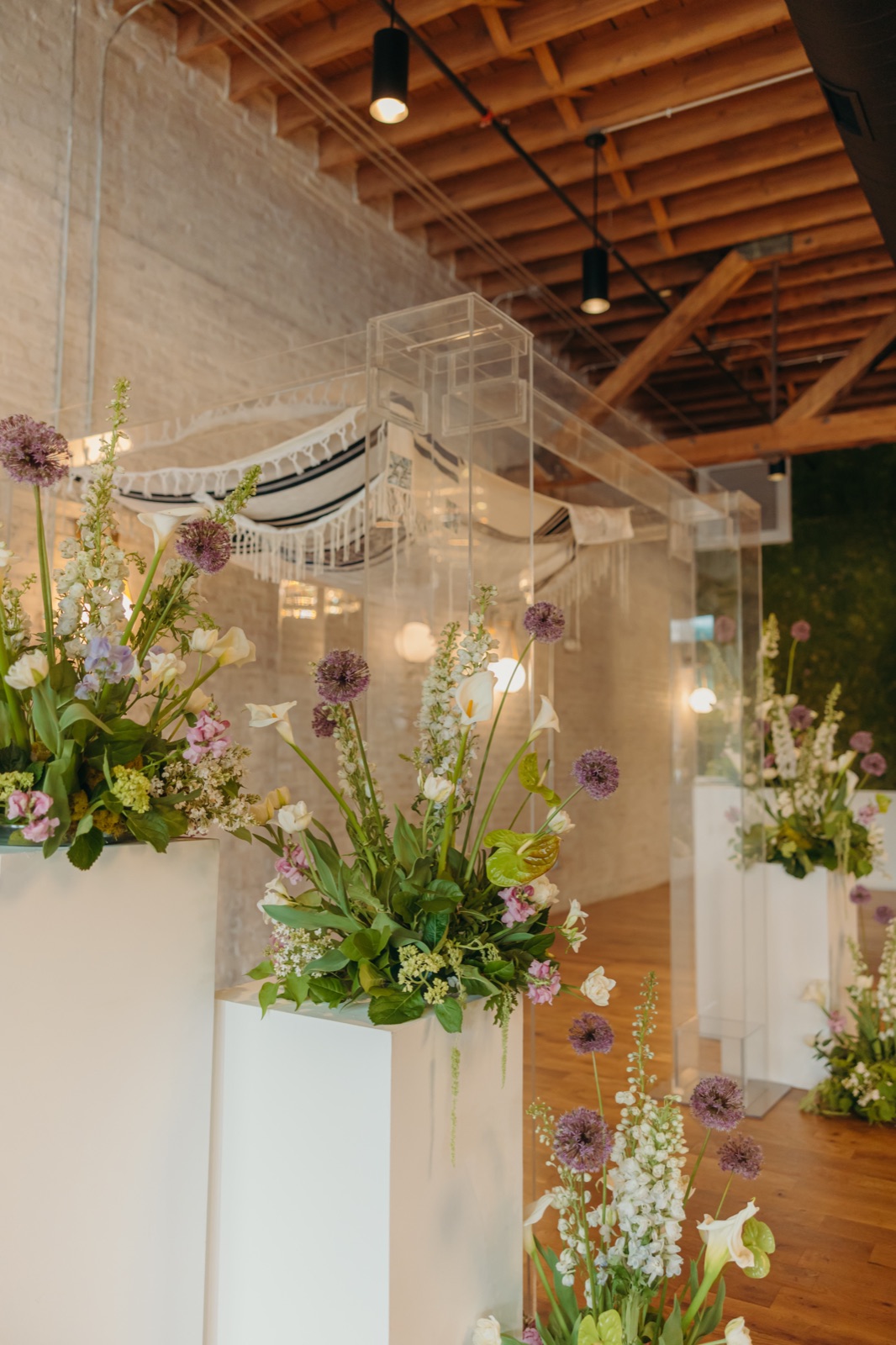 The clear acrylic chuppah with a tallit canopy above floral pedestals