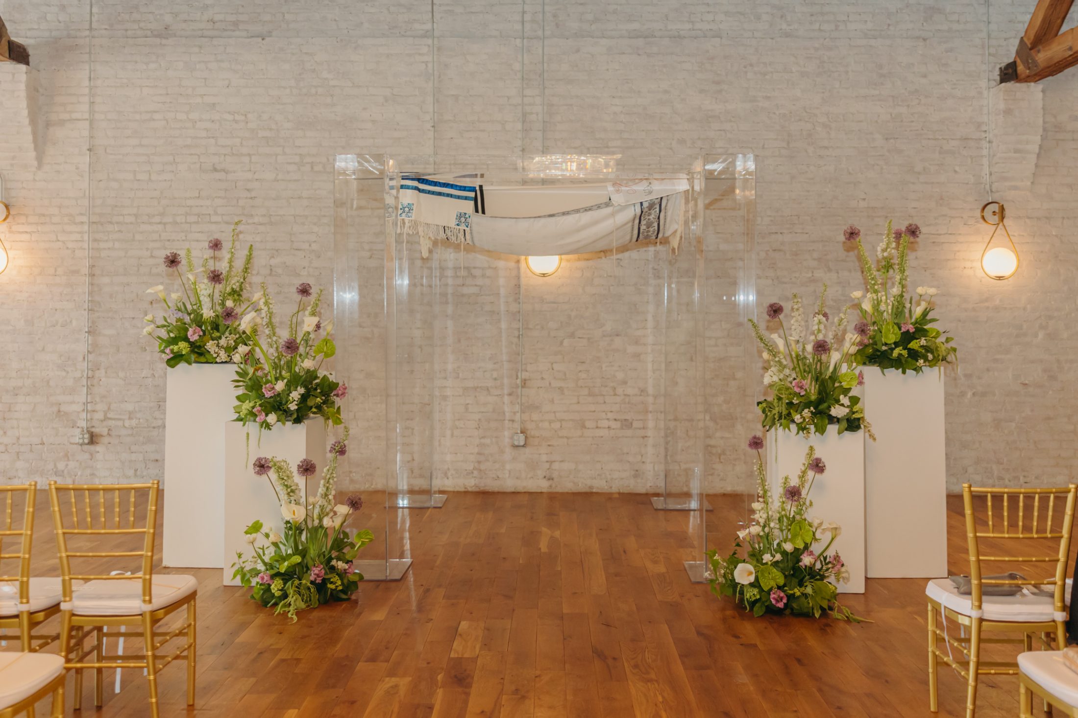 The clear acrylic chuppah with a tallit canopy and floral pedestals
